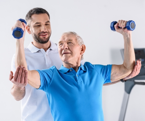 rehabilitation therapist assisting senior man with dumbbells